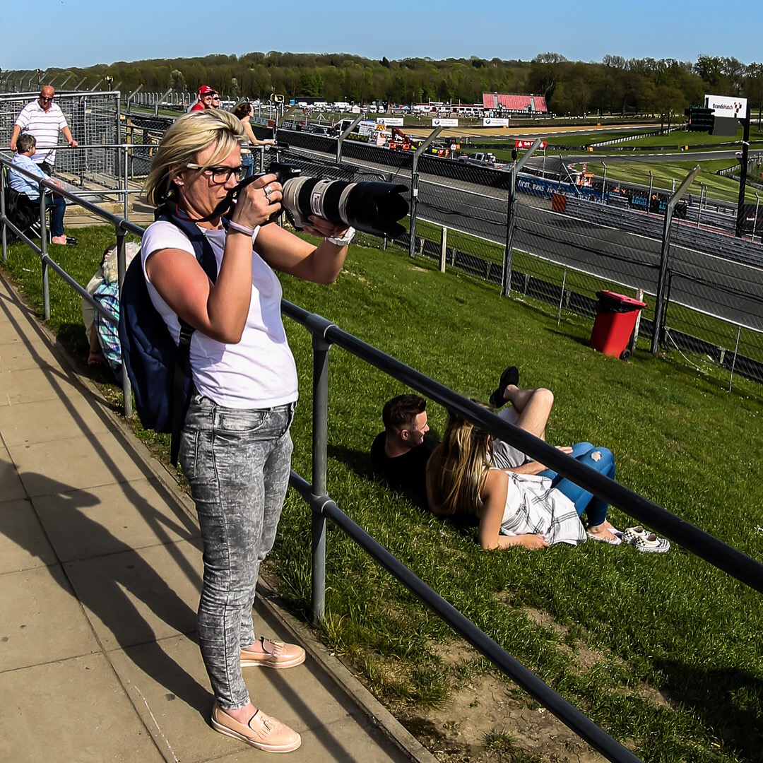 Natalia framing a shot trackside, telephoto extended toward the start-finish straight.